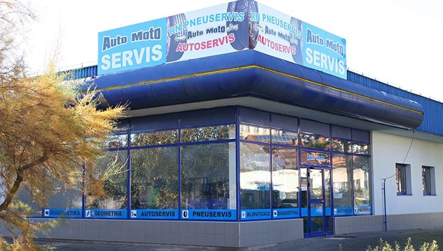 Prosklená budova servisu s modrou střechou a nápisy Auto Moto Servis, Pneuservis, Autoservis
